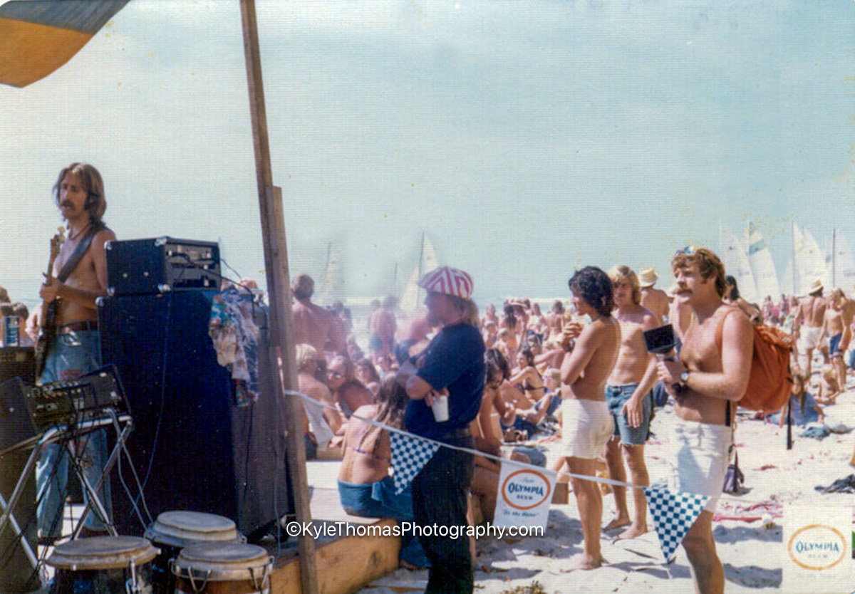 Behind the stage at the 1975 Stonesteps Surfing Contest — band mid-set, Olympia Beer pennant line, sailboats