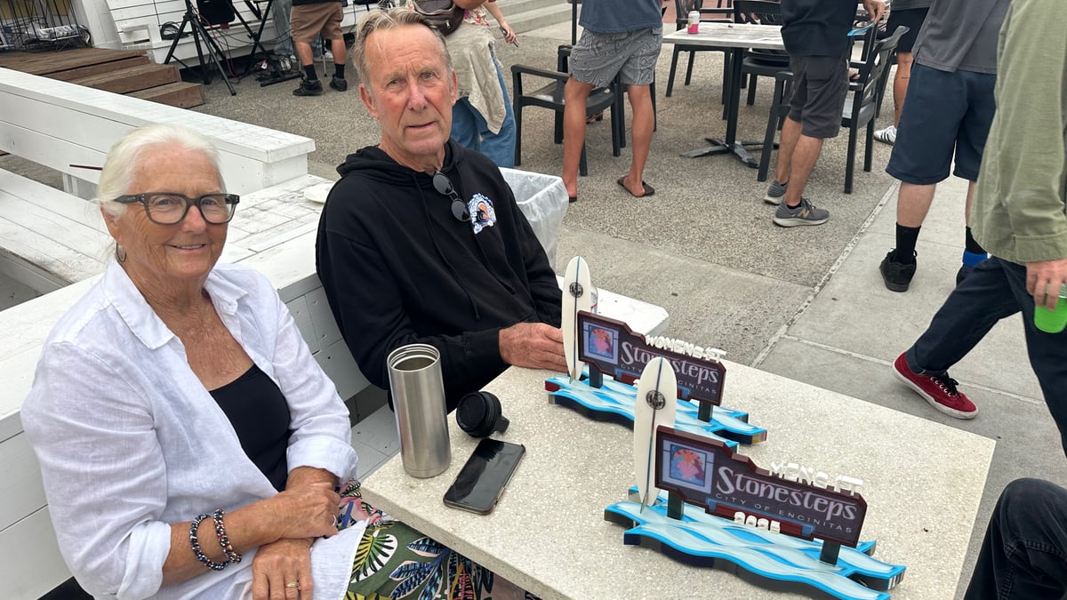 Muffy and John Peugh seated at a table at the 2025 Stonesteps Surfing Contest with two trophies in front of them