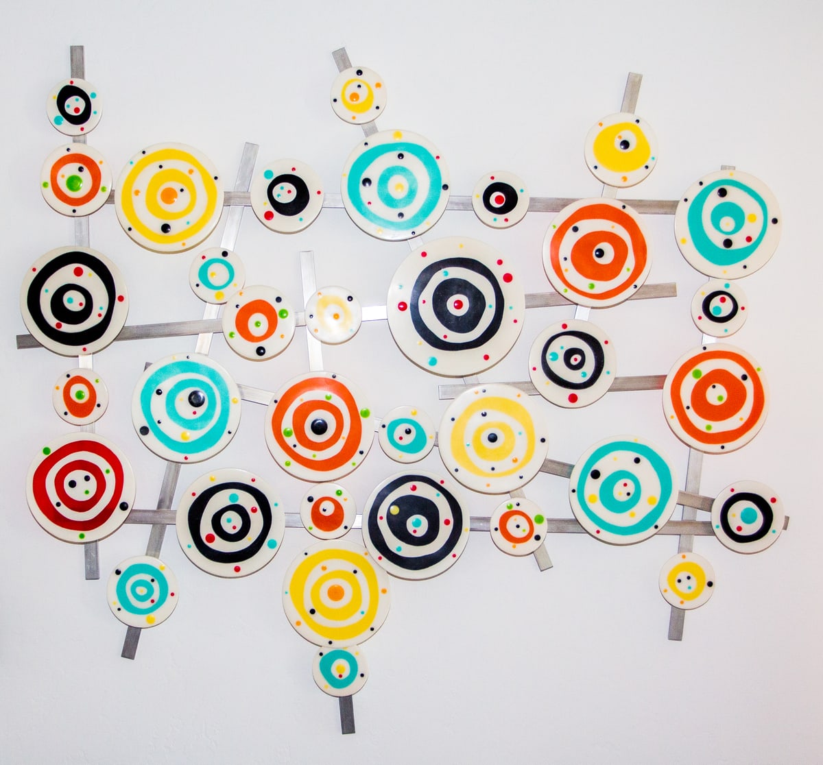 A wall sculpture of brightly coloured concentric-circle resin discs mounted on brushed metal bars