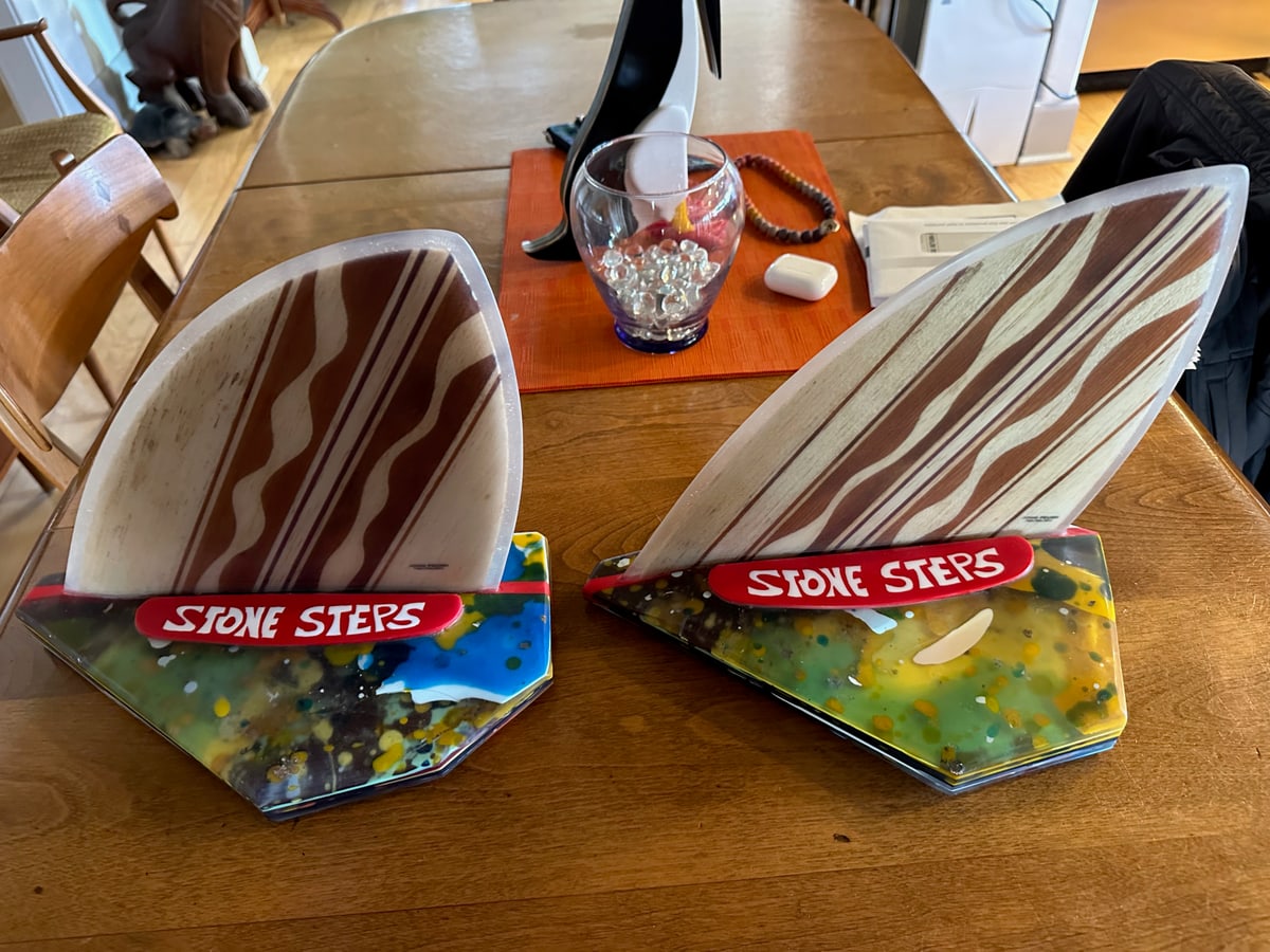 Two Stone Steps trophies on a wooden table, wooden surfboard fins rising from speckled resin bases