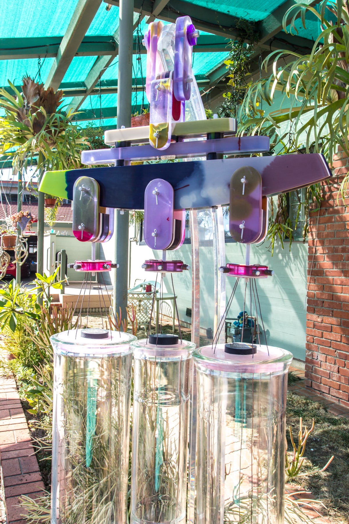 Wind chimes of translucent resin and glass tubes hanging under a shade structure in a garden