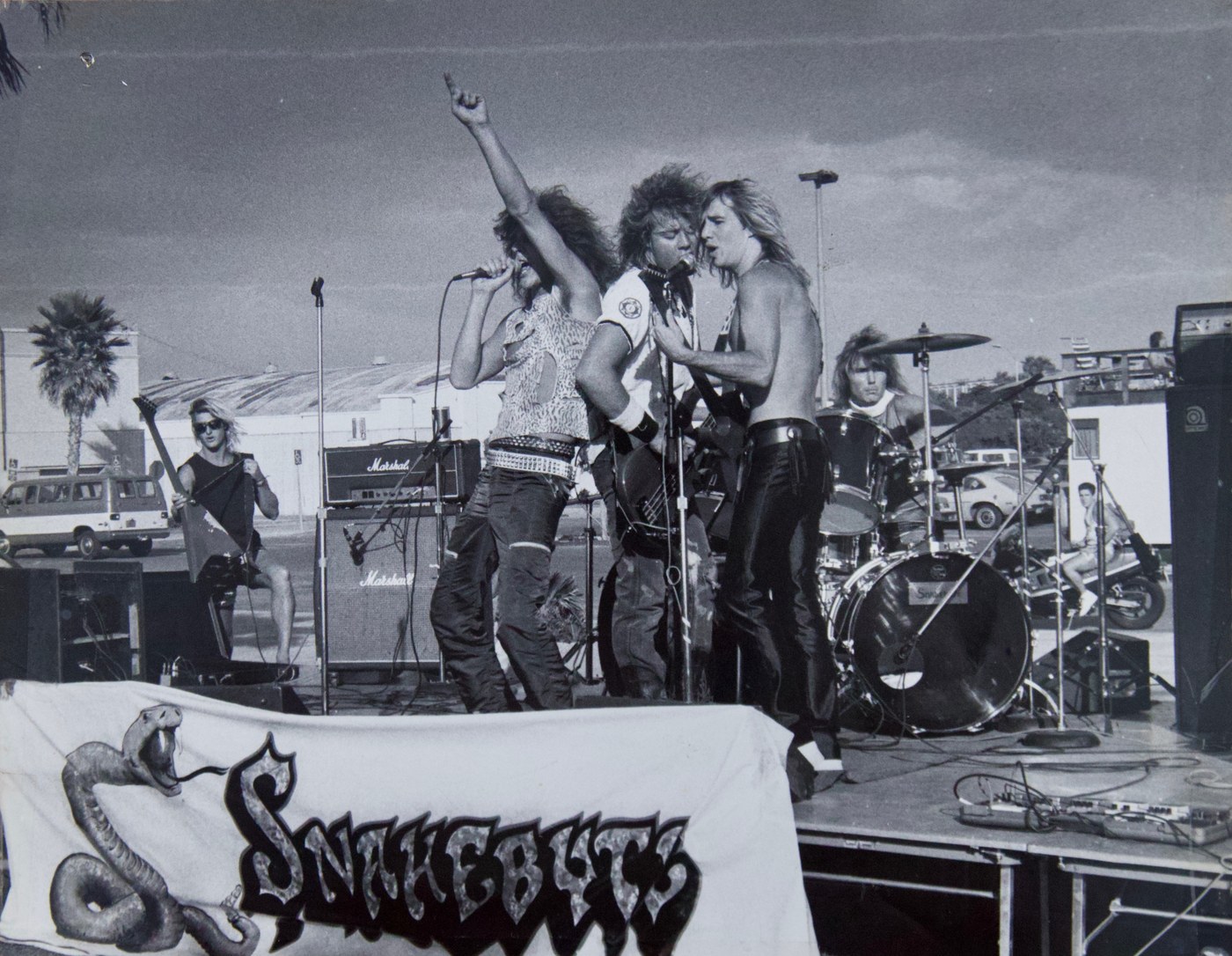 Snakebyte performing on an outdoor stage outside Belmont Park with the band banner on the barricade