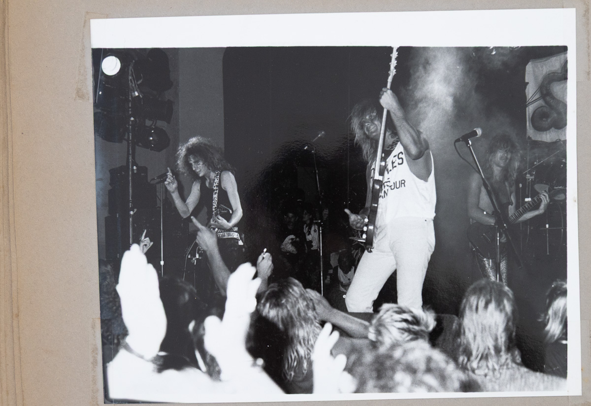A black and white print in a scrapbook showing a band on stage with hands raised in the crowd at the front