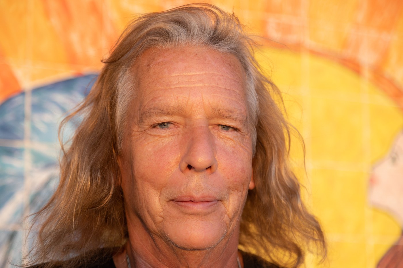Wally Passet looking into the camera against the orange painted backdrop, 2021