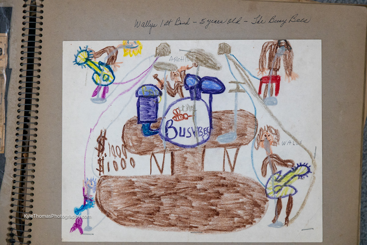 A child's crayon drawing of a band on stage, pasted in a scrapbook, captioned Wallys 1st Band 5 years old The Busy Bees