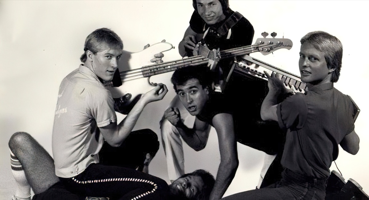 Black and white publicity photo of the band Bratz, four members clowning for the camera, one holding a bass guitar over his shoulder