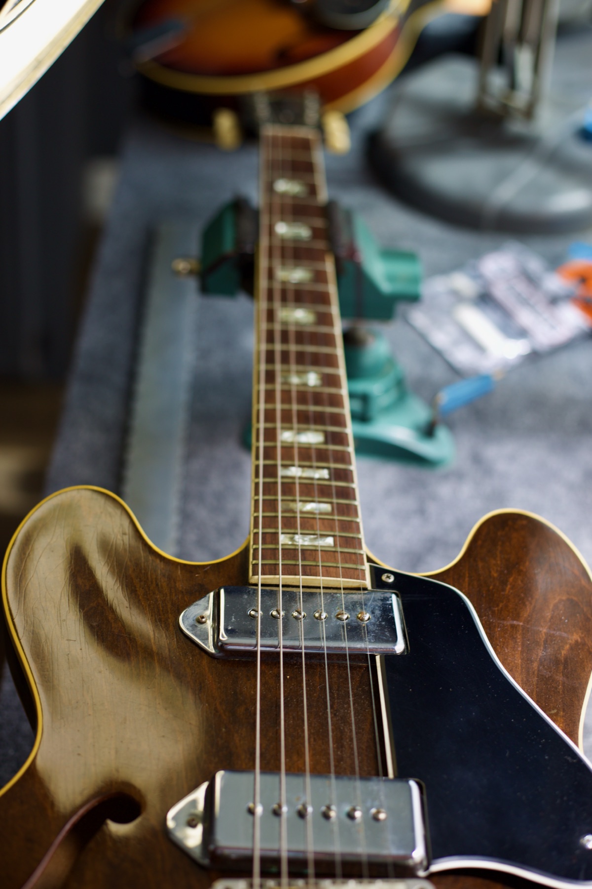 Looking down the fretboard of a walnut archtop guitar clamped on the workbench, mother-of-pearl block inlays receding toward the headstock
