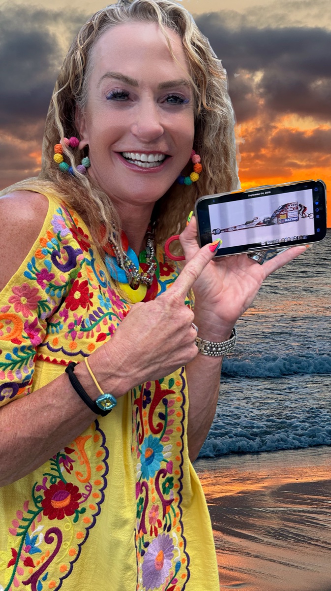 Denise Mueller at sunset on the beach holding up her phone showing the record run on the salt flats