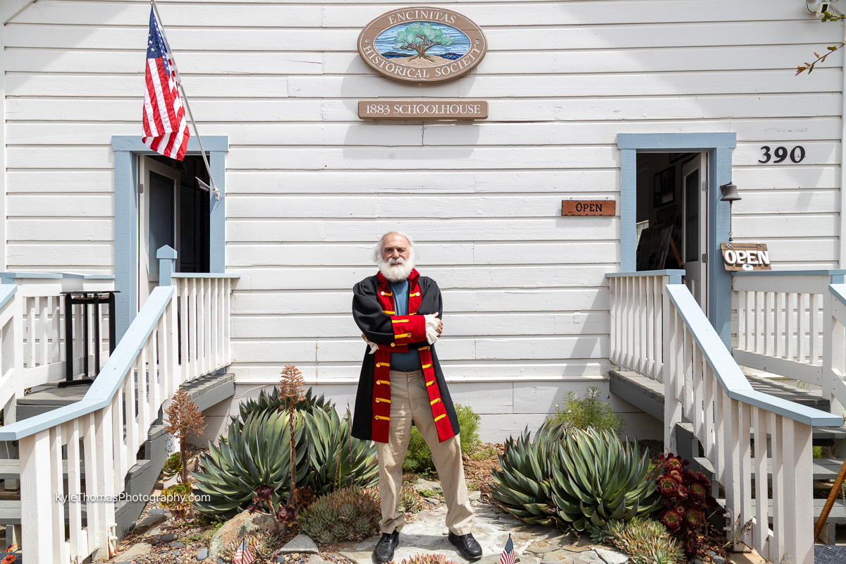 Hillel Schwartz in a colonial coat, arms crossed, outside the 1883 Schoolhouse